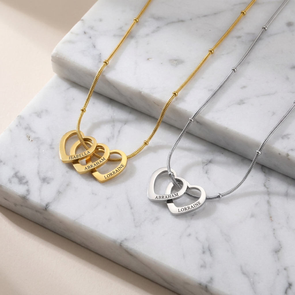 Two personalised heart necklaces side by side, one gold and one silver, each heart engraved with a name