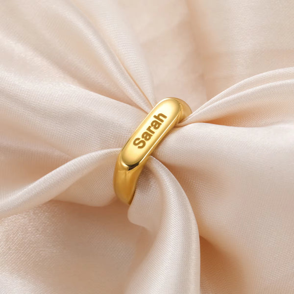 Personalised gold ring engraved with a name, resting on cream silk